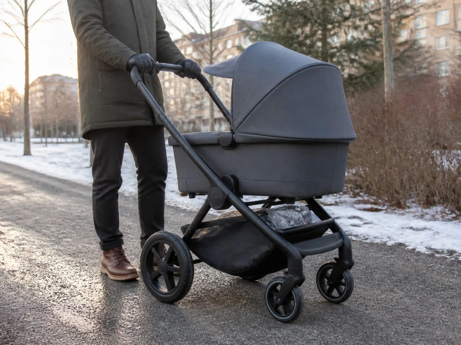 Barnvagn med sufflett på en gångväg där sol och lätt snö visas i två delar.