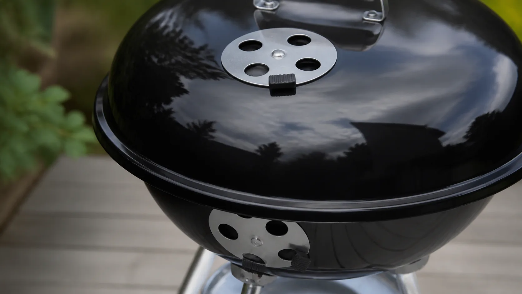 Hand som justerar luftspjället på en kolgrill med lock.