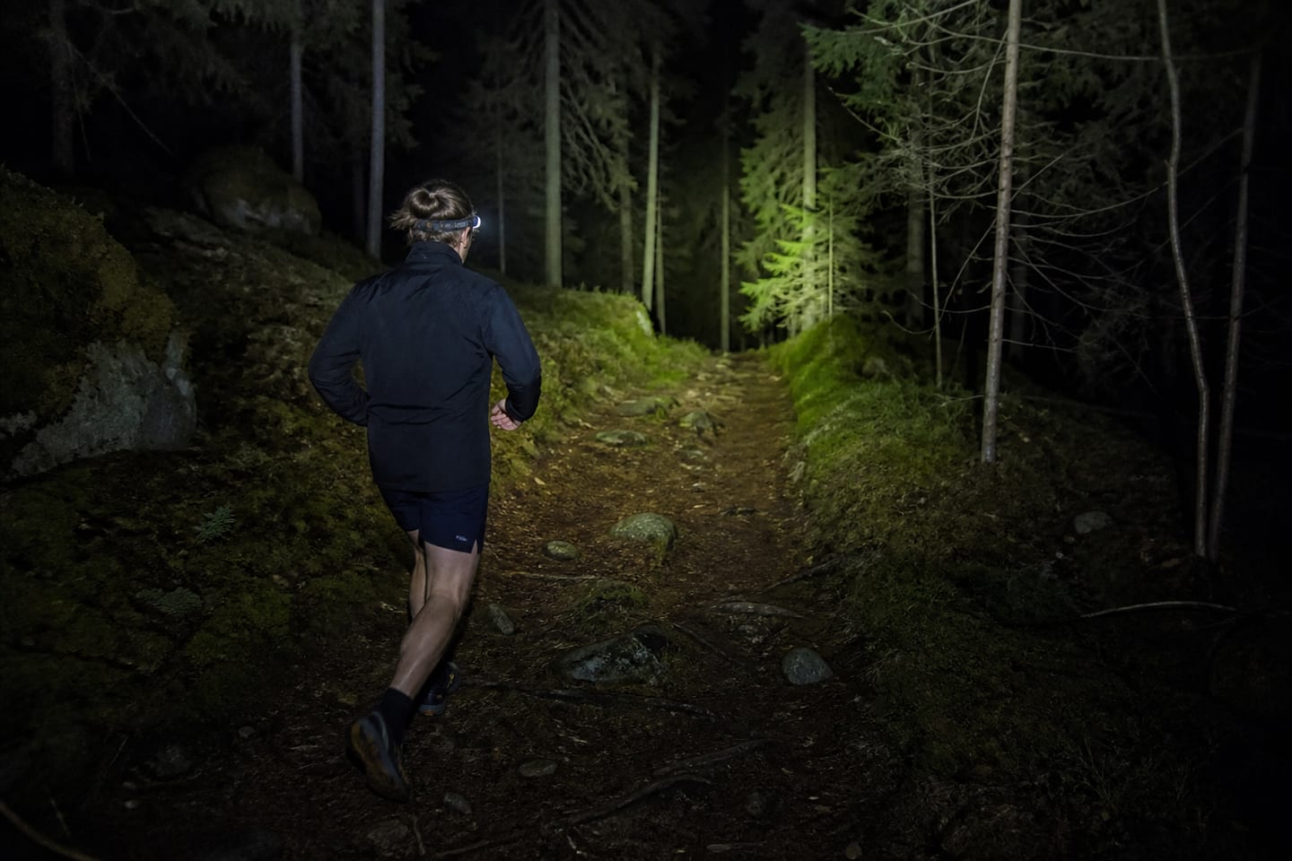 Löpare med pannlampa på skogsstig i mörker.