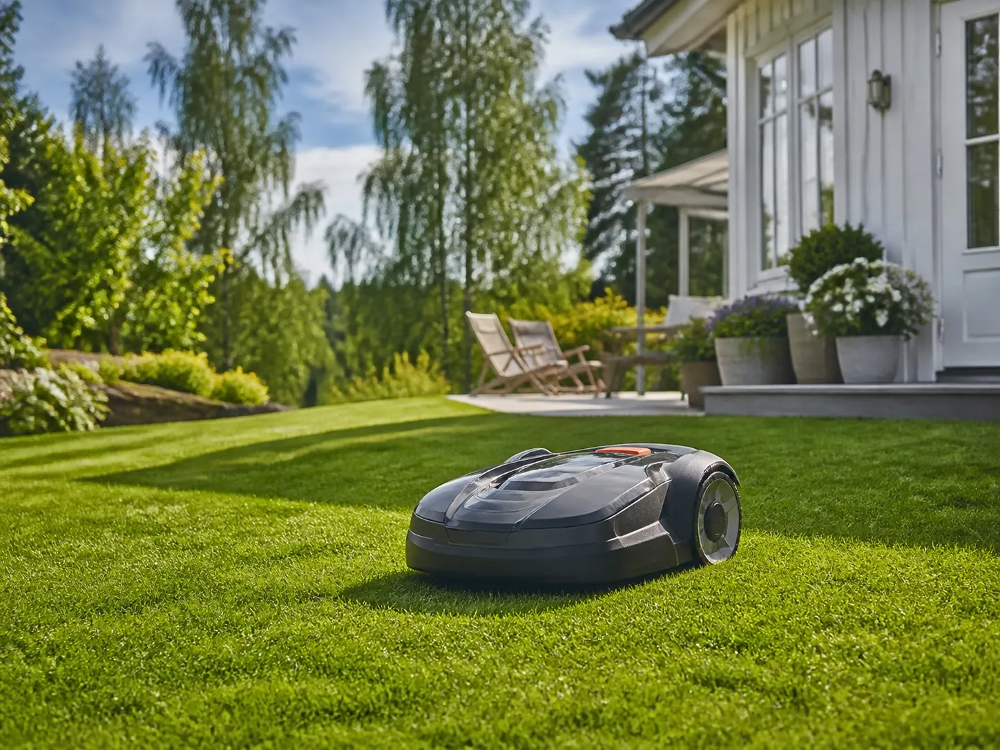Robotgräsklippare på en svensk villagräsmatta med rabatt och träd i bakgrunden.