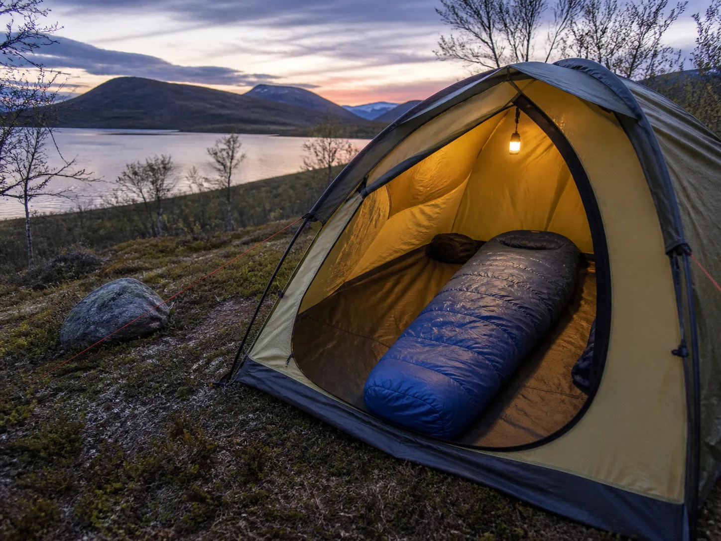 Sovsäck i ett öppet tält vid en svensk fjällsjö i kvällsljus.